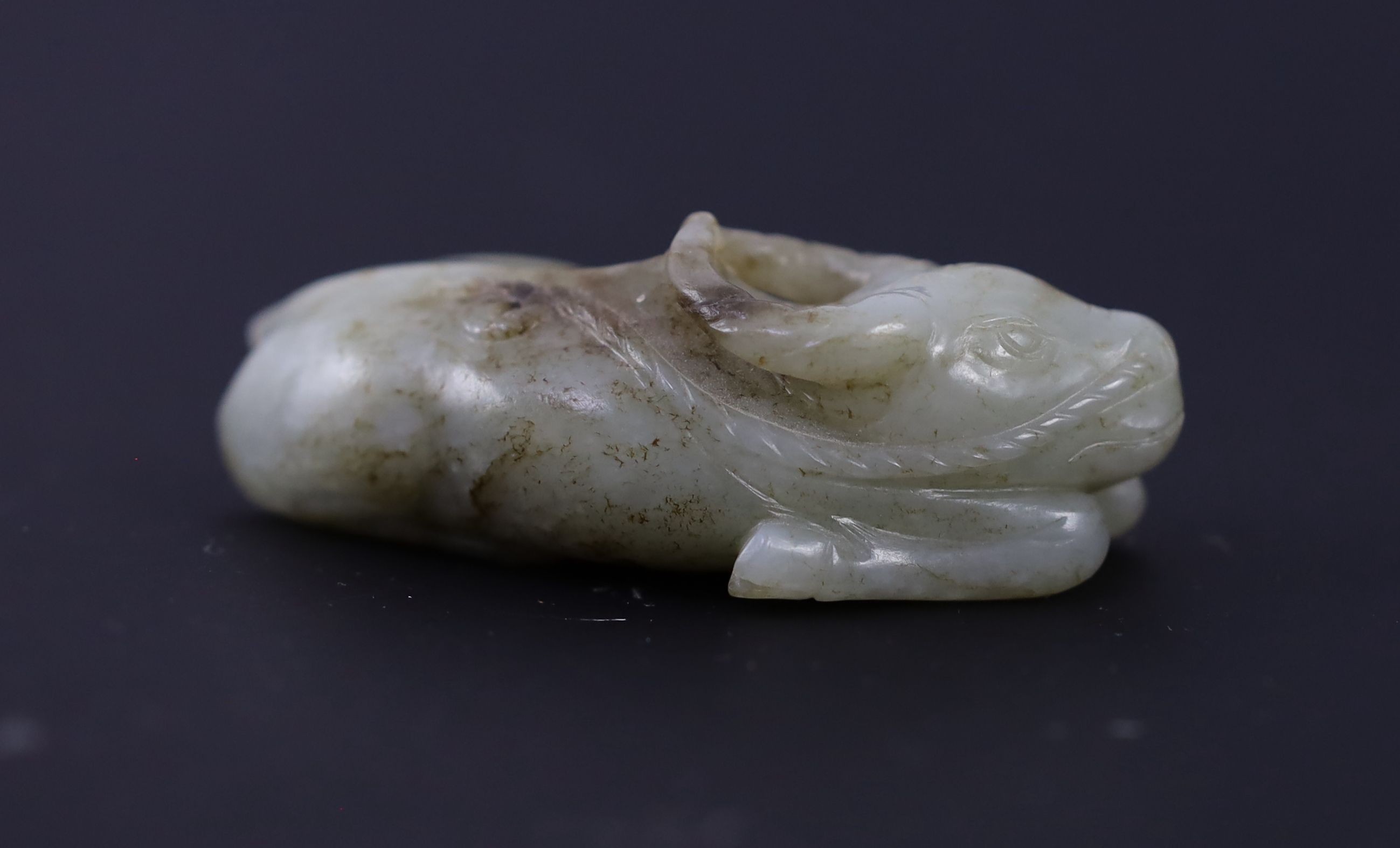 A Chinese Ming pale celadon and brown jade figure of a recumbent Buffalo, 16th/17th century, 8cm long